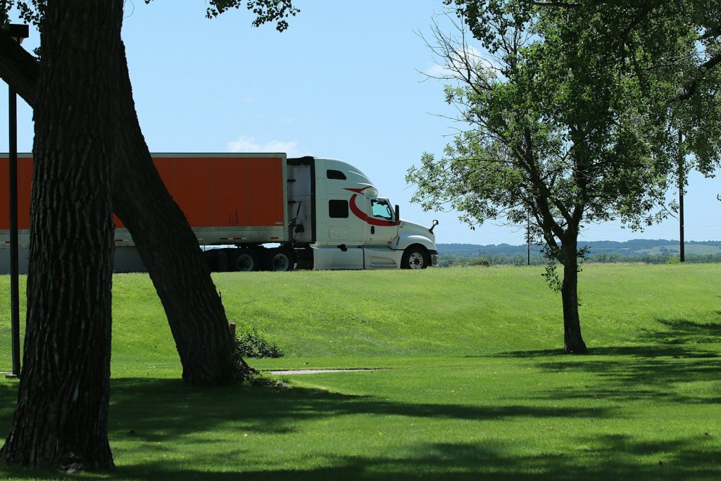 White semi-truck with orange trailer drives on road.